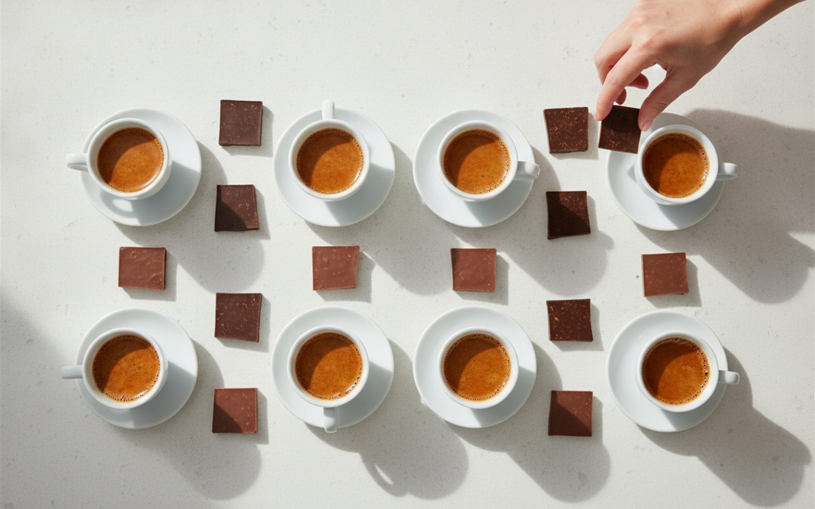 Espresso cups and squares of dark and milk style chocolate lined up for a blind taste test on a bright kitchen counter